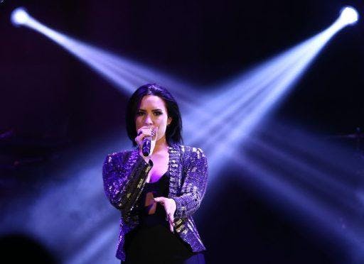 Demi Lovato in a sparkling cardigan performing on stage.