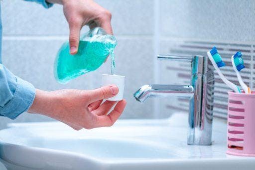 A person pouring mouthwash into a cup over a sink.