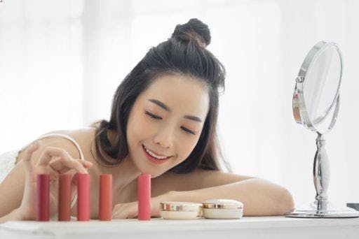 Woman smiling and touching a one of several tubes of lipsticks.