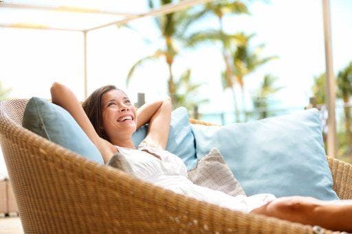 Woman happily relaxing on a wicker lounge chair outdoors.