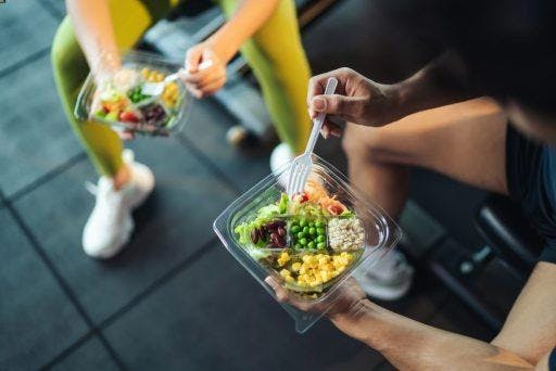 Cropped image of woman and man eating healthy food at the gym. 