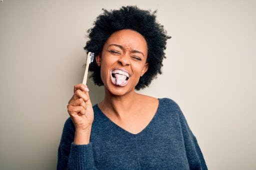 A woman holding a toothbrush while showing her tongue.
