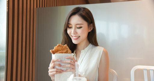Smiling woman looking at breaded meat in a paper bag.