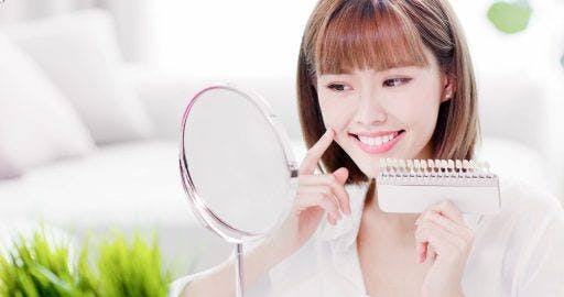Woman smiling in the mirror holding teeth colour samples. 