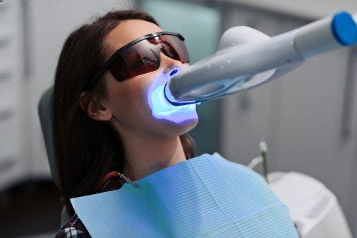 Top view of a woman in a dentist chair with blue light pointed at her teeth. 