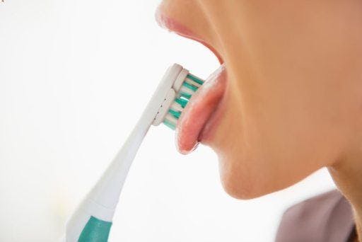 Cropped photo of a woman brushing her tongue with a toothbrush.