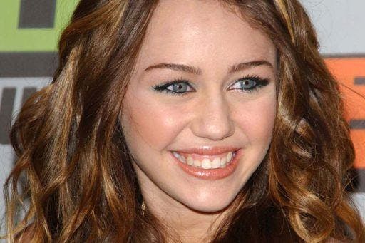 Miley Cyrus smiling against a backdrop of a charity event.