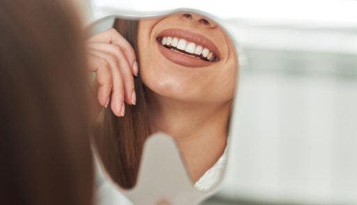 Close-up of woman smiling and checking her teeth in a mirror.