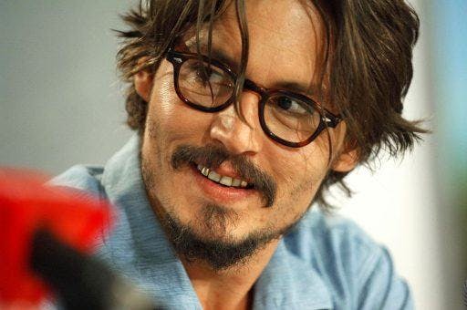 Johnny Depp in glasses smiling with a gold tooth.
