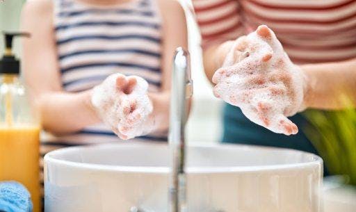 Close-up of a kid and an adult in stripes washing their hands with soap.