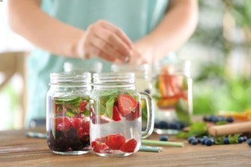 Mason jars with berry-infused water with blurred image of a woman in the background.