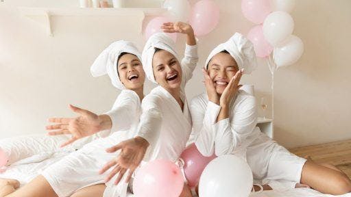 Smiling women in white robes with visible pink and white balloons.
