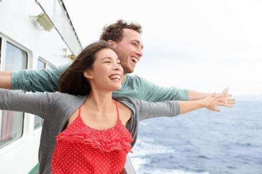 Couple on a ship happily spreading their arms. 