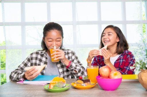 Two teenage girls happily eating sandwiches and juice.
