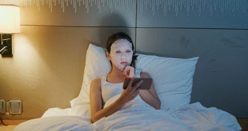 Woman in wearing sheet mask and watching on her handheld device.