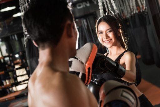 Smiling woman boxing with a coach at the gym.